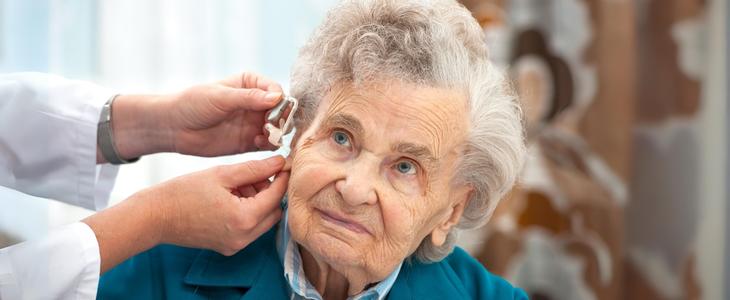 featured image used for the blog post, understanding hearing impairment. doctor examining an older woman and fitting her with a hearing aid.